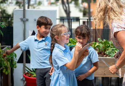 Year 2 children from T3 2024-25 discussing measurements with their teacher in the outdoor learning area.