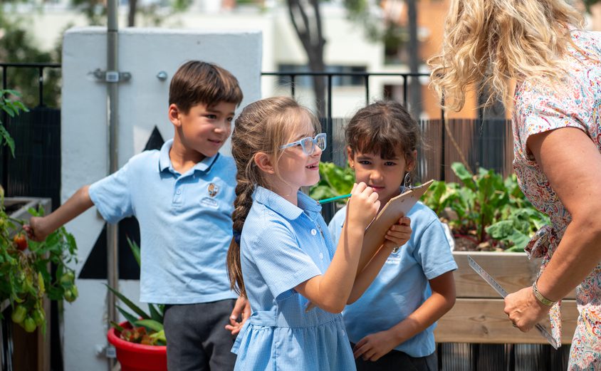 Year 2 children from T3 2024-25 discussing measurements with their teacher in the outdoor learning area.