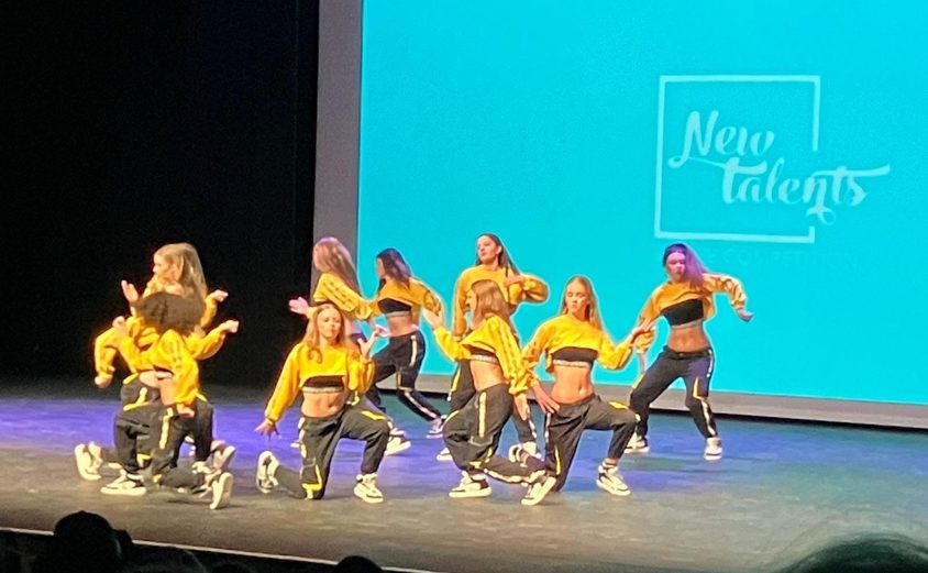 Group of dancers in yellow tops and black sweatpants performing on stage
