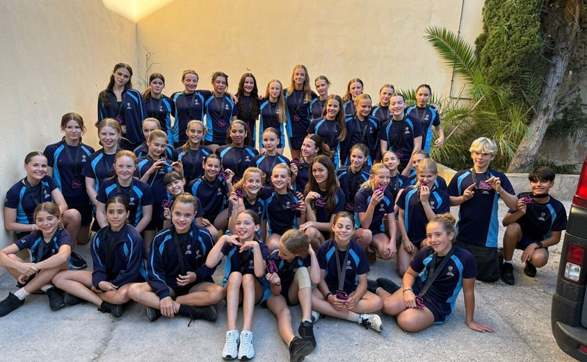 Group of dancers sitting smiling at the camera in sports clothes