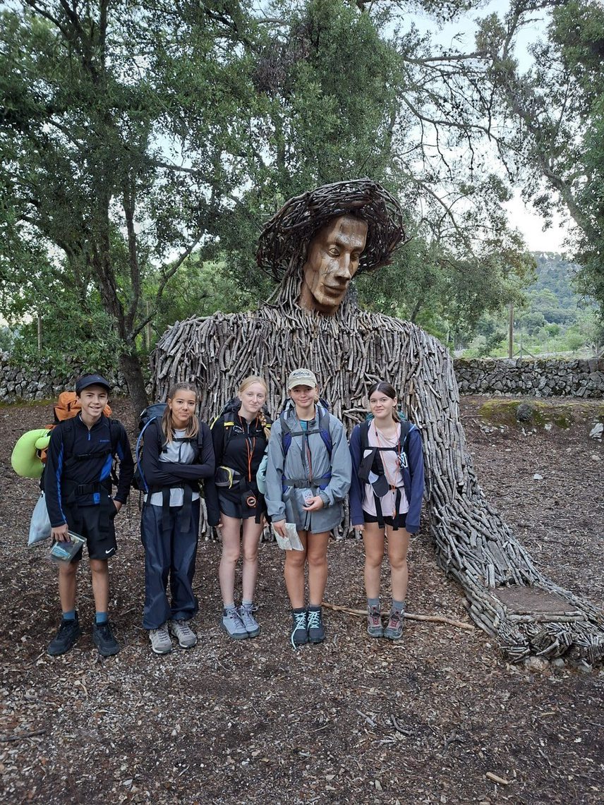 Dof E 5 hikers with backpacks on standing and smiling in front of a tree type statue