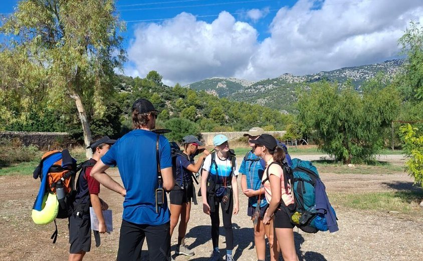 Dof E 5 hikers wth backpacks on in a circle getting briefed by their guide