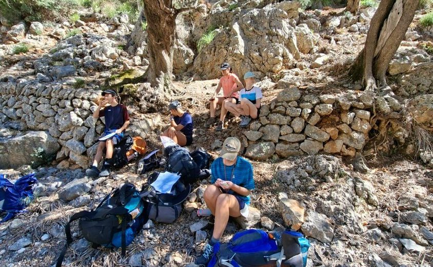 Dof E five hikers with backpacks on the ground having a lunch break