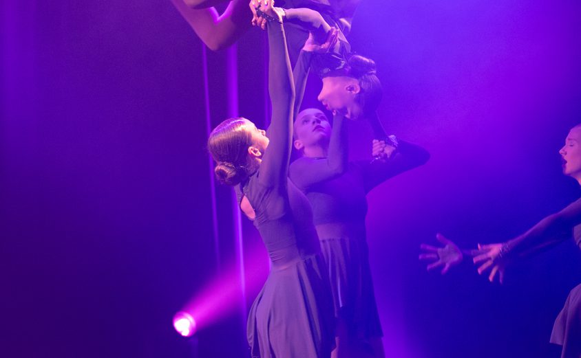 A girl held up as she somersaults by two other girls mid dance