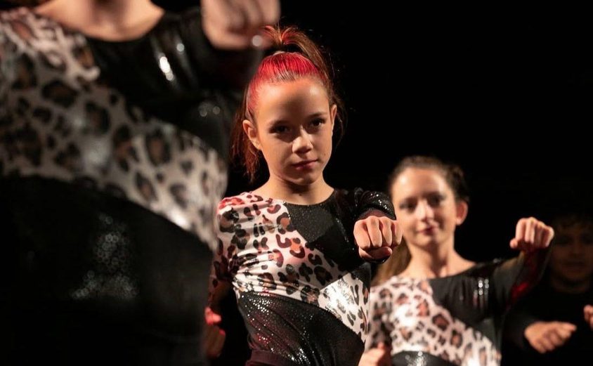 Girls in leopard print leotards with arms in punching motion on stage