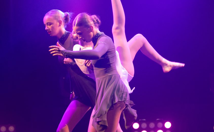 Two girls carrying another girl in serious pose on stage