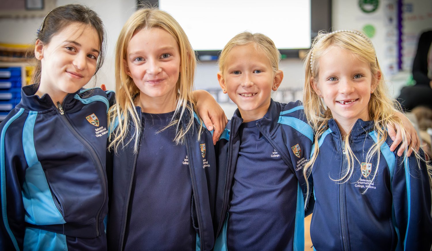 Four Year 3 girls smiling with arms around shoulders in a classroom