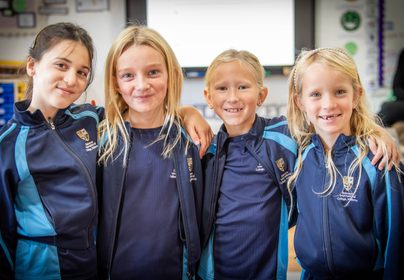 Four Year 3 girls smiling with arms around shoulders in a classroom