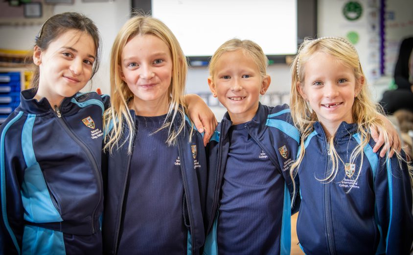 Four Year 3 girls smiling with arms around shoulders in a classroom