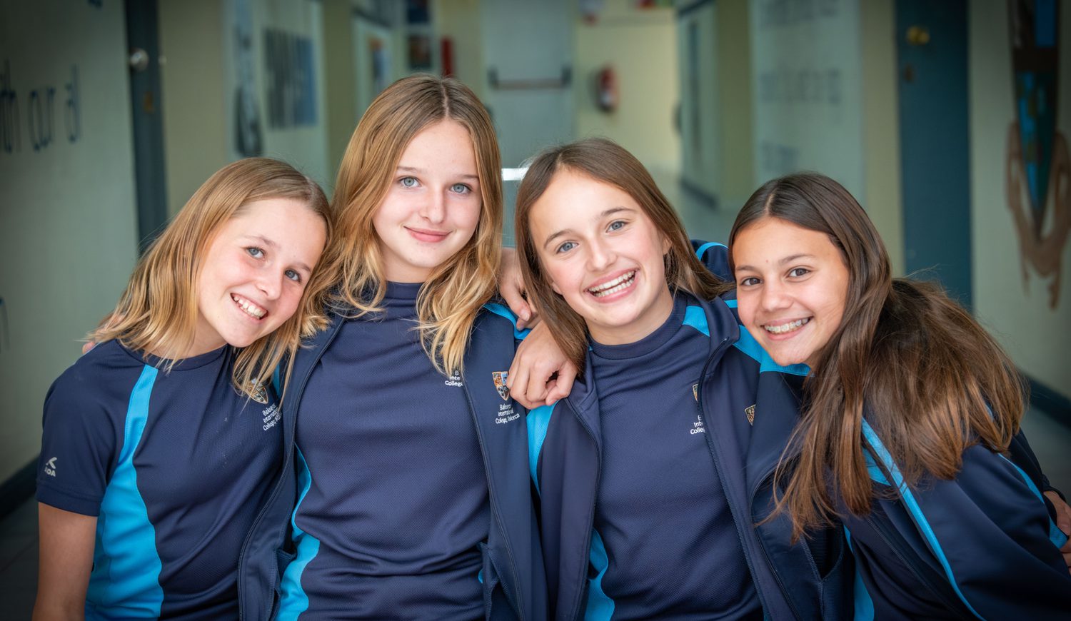 Four secondary girls smiling at the camera in the corridor