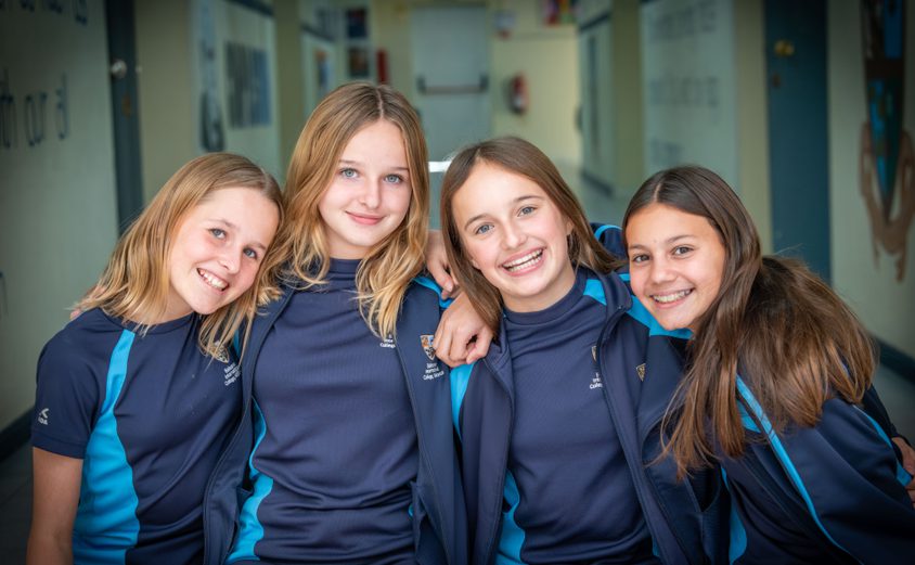 Four secondary girls smiling at the camera in the corridor