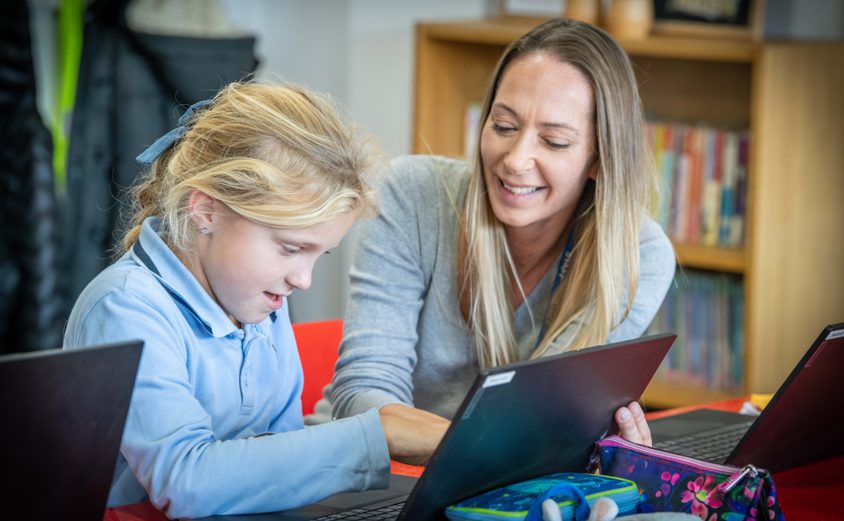 Primary teacher helping a Year 4 girl on a laptop