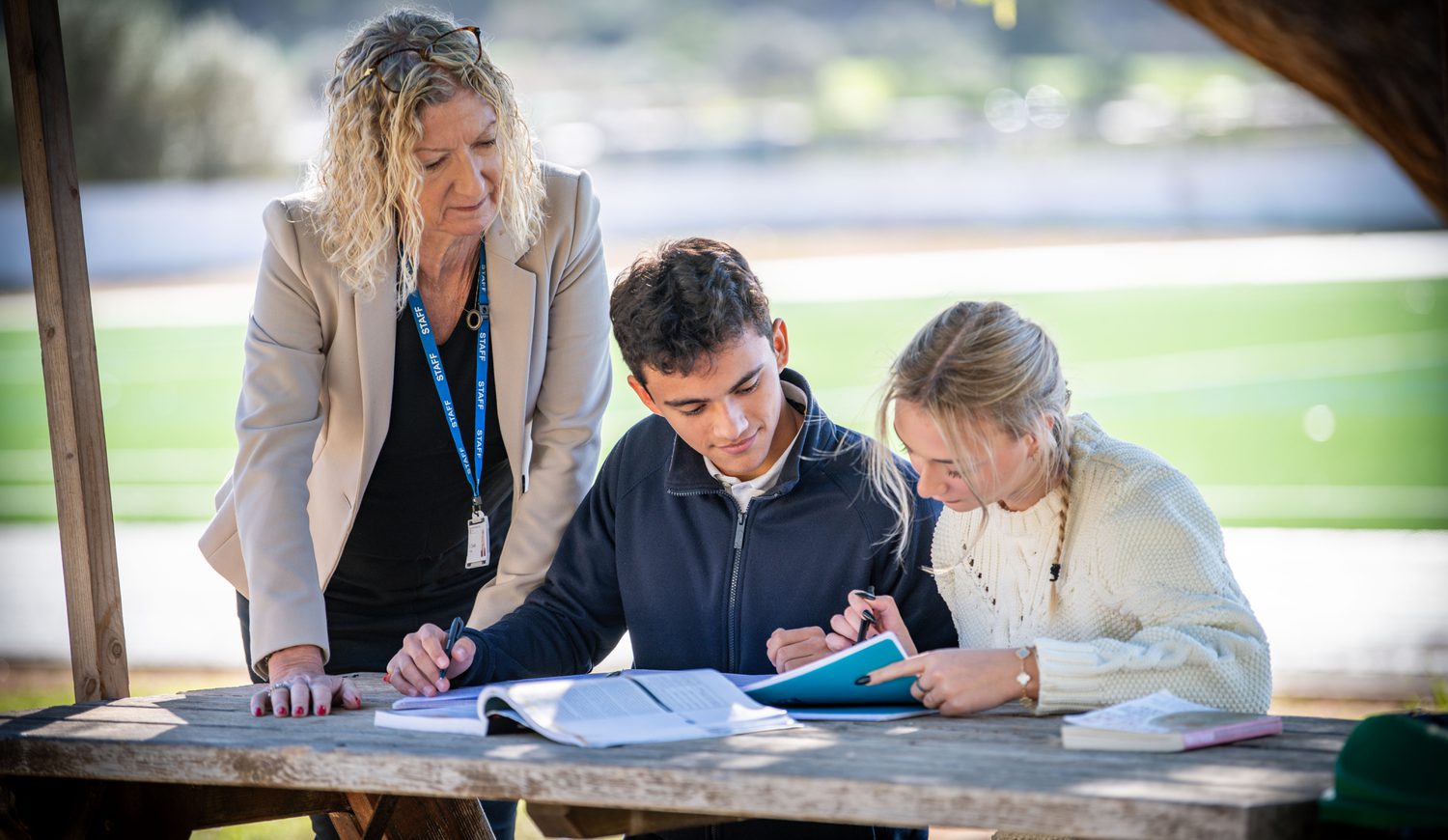 Principal leaning over looking at two Sixth Form students working outside on a bench