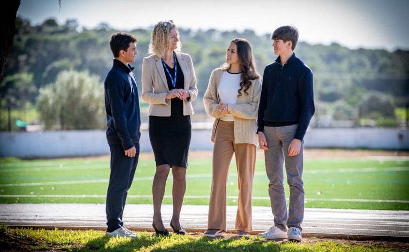 Principal standing talking to three Sixth Formers outside with Astro Turf in background