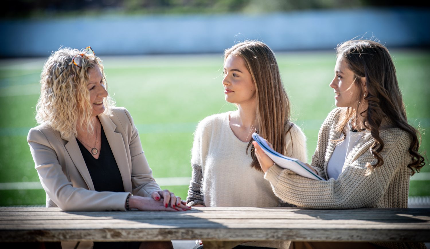 Principal talking to two Sixth Form girls on a bench in front of Astro Turf