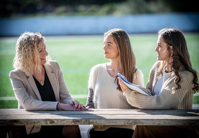 Principal talking to two Sixth Form girls on a bench in front of Astro Turf