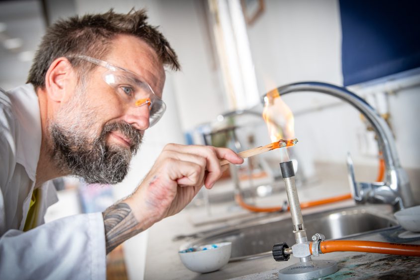 Science teacher with goggles on lighting a bunsen burner