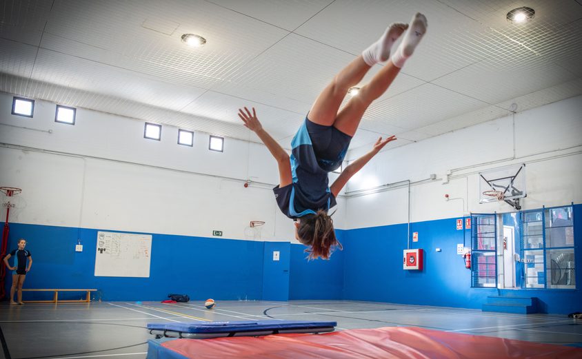 Secondary girl doing a somersault onto a gym mat in the sports hall