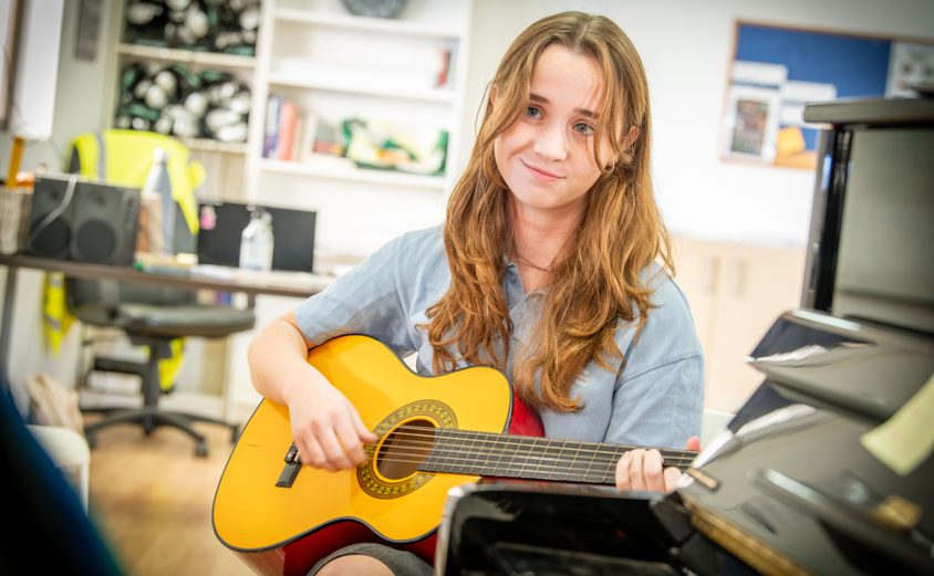 Secondary girl playing the guitar on a chair