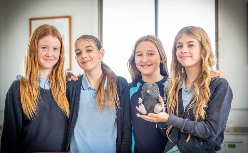 Secondary girls smiling at the camera with a mole in the science lab