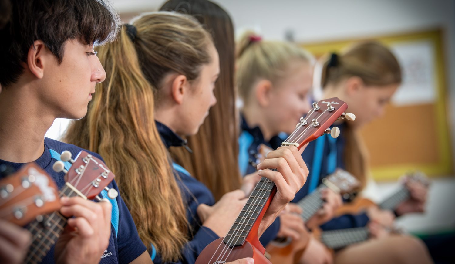 Secondary students on the ukuleles in a row looking away
