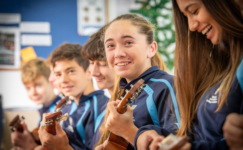 Secondary students playing the ukulele and smiling