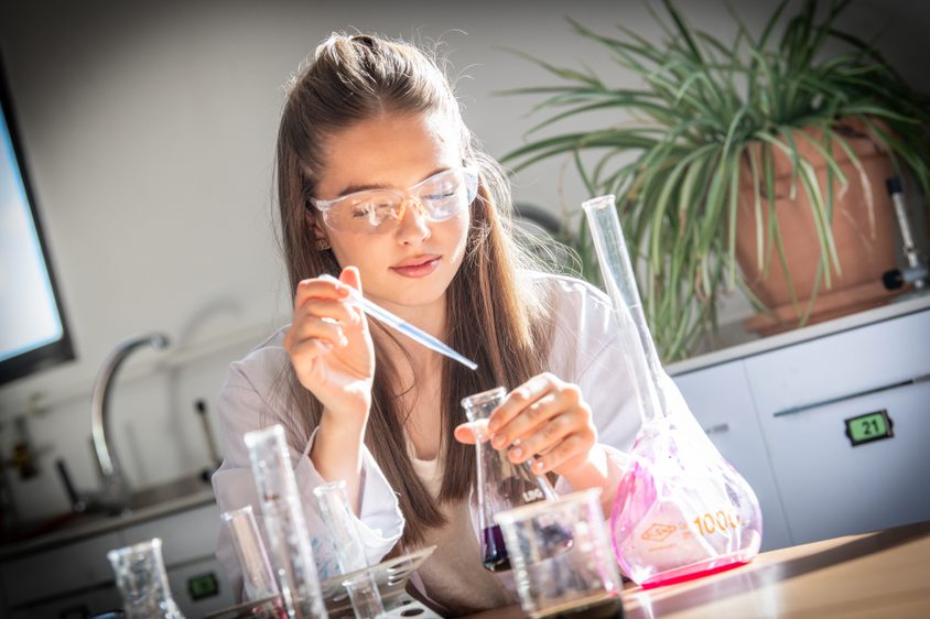 Sixth Form Girl dropping chemicals into a beaker with a dropper in school science lab