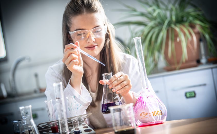 Sixth Form girl dropping chemical liquid into a beaker in science lab