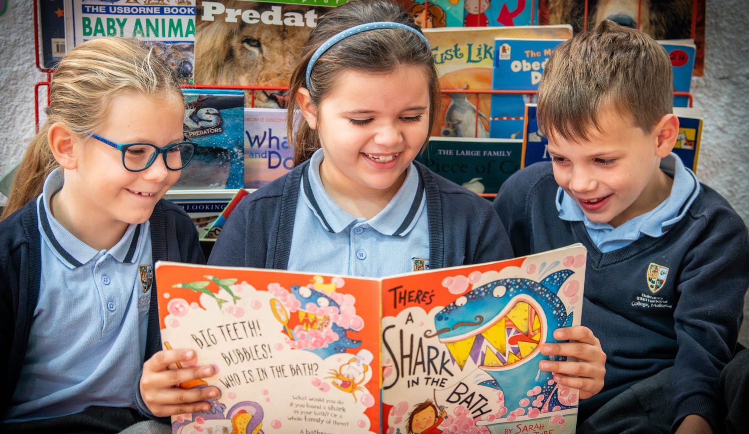 Three Primary children smiling while reading a book in the reading corner