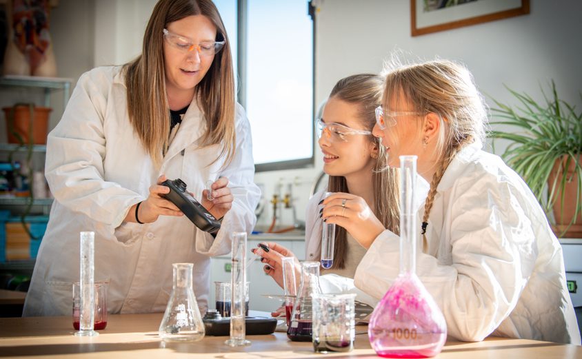 Two Sixth Form girls holding a test tube and looking at their science teacher