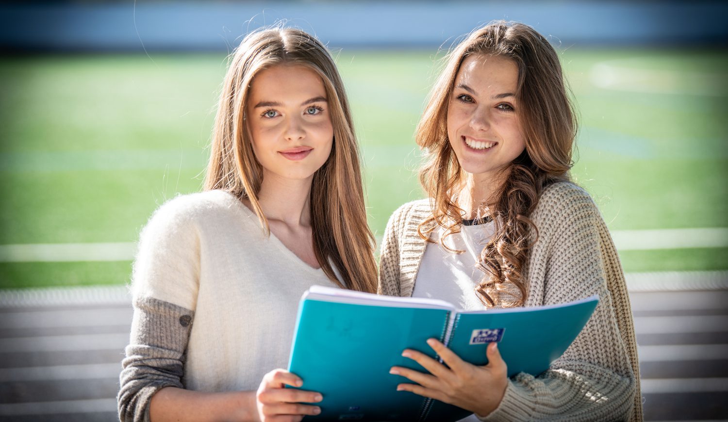 Two Sixth Form girls smiling at the camera with a book they are sharing