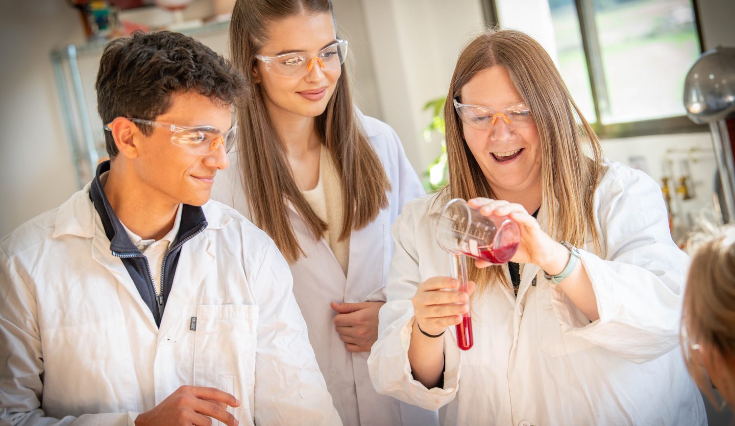 Two Sixth Form students watching a teacher pouring liquid into a tube in the science lab