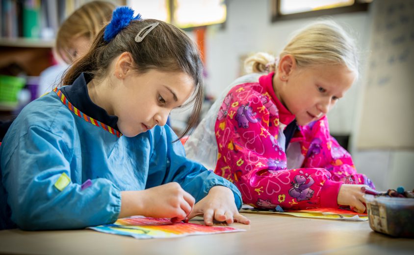 Two Year 3s in painting jackets colouring in at a table