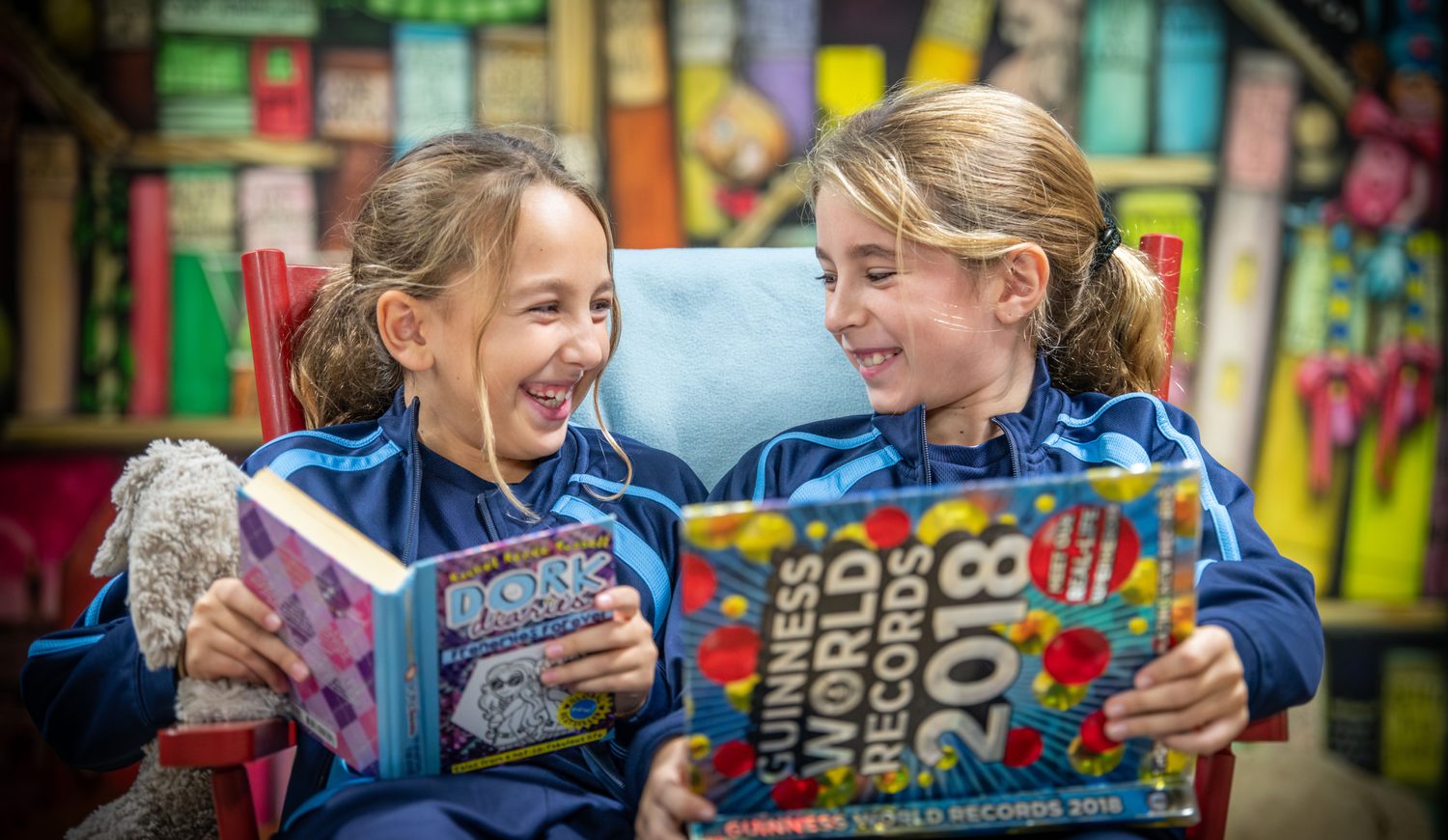 Two Year 5 girls laughing while reading books on a chair in the library