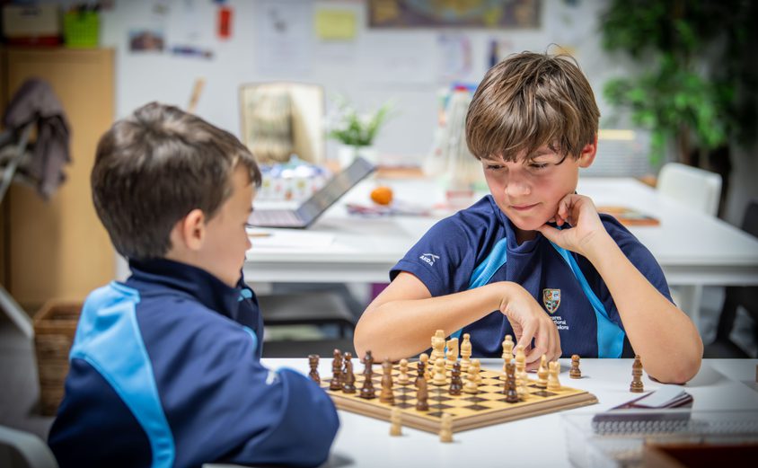Two primary boys playing chess in the library