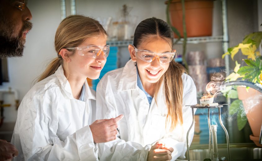 Two secondary girls smiling at an experiment with the teacher in science lab