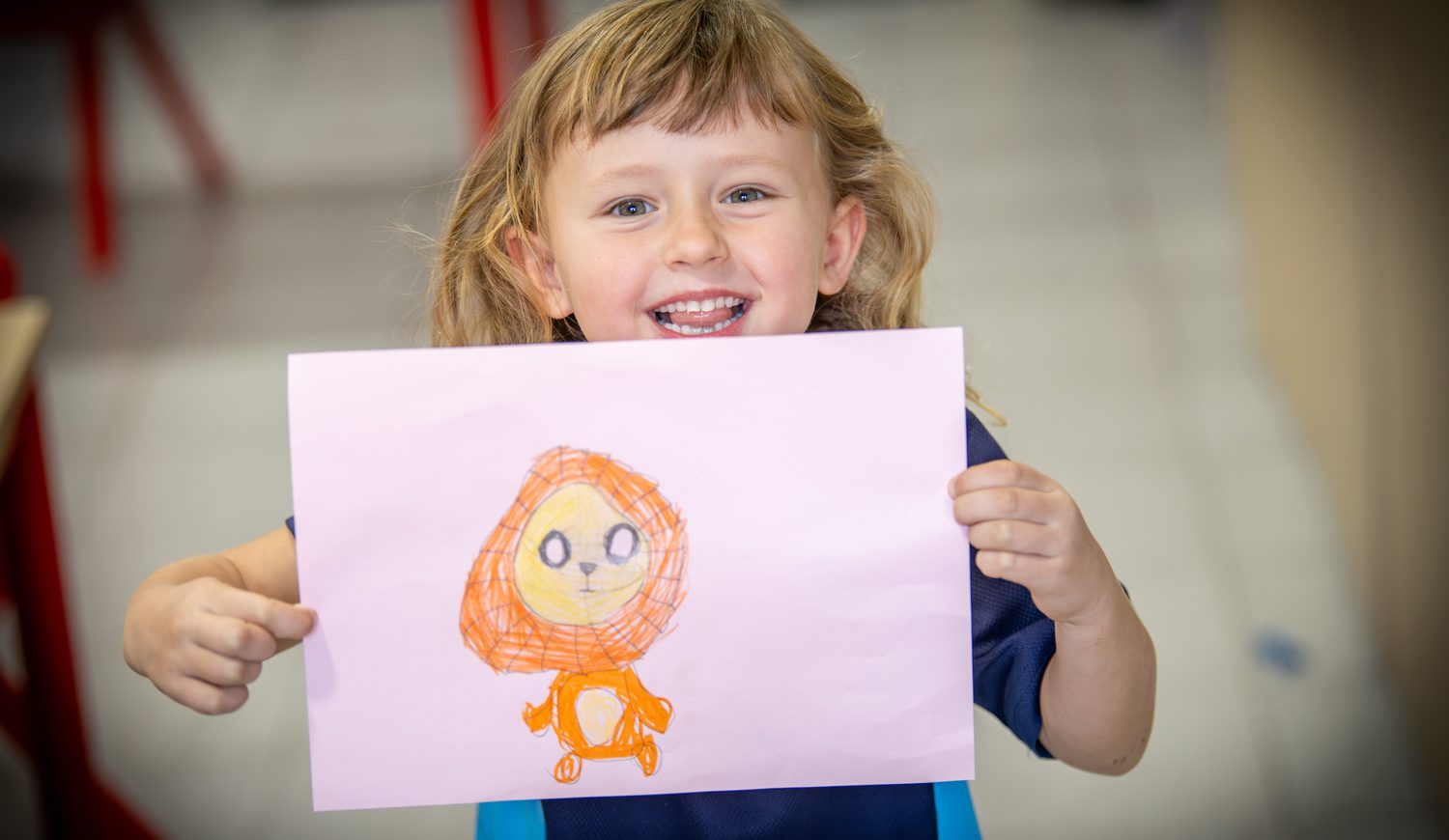 Year 1 girl proudly showing her art of a lion with a big smile on her face