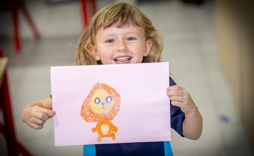 Year 1 girl proudly showing her art of a lion with a big smile on her face
