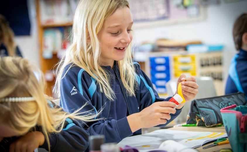 Year 3 girl applying glue stick to a paper at her desk