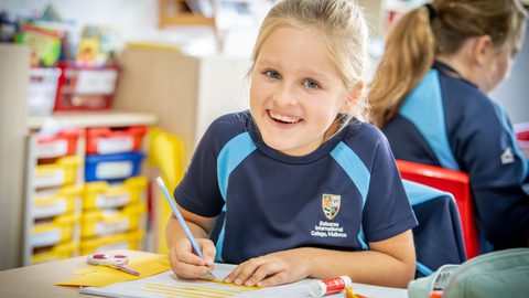 Year 3 girl working at her desk looking up and smiling