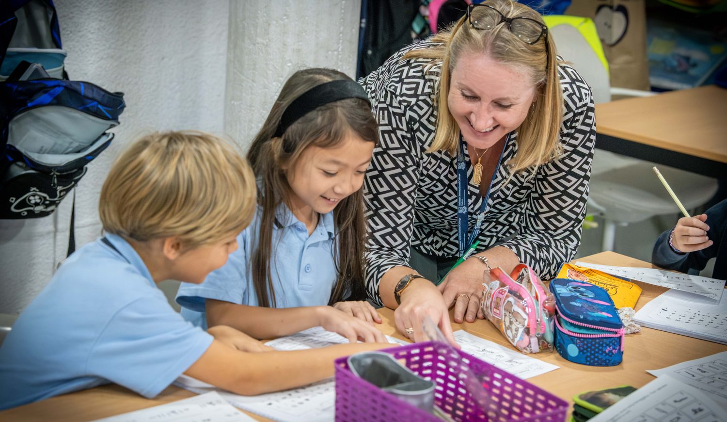 Year 4 teacher leaning over at a desk helping two students with their work