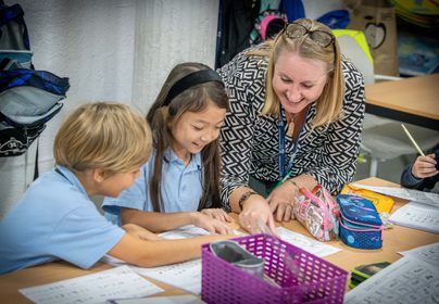 Year 4 teacher leaning over at a desk helping two students with their work
